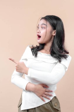 Şaşırmış genç bir Asyalı kadın, heyecan ve merak gösteren, heyecan ve ilgi kavramları için mükemmel bir yüz ifadesiyle yan tarafları işaret ediyor..