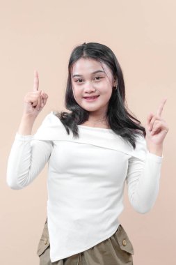 Neşeli, genç Asyalı bir kadın güvenle gülümserken iki elini de yukarı kaldırarak yeni fikirleri, yaratıcılığı, ilhamı ve günlük iş ve iş hayatında olumlu bir görünümü sembolize ediyor..