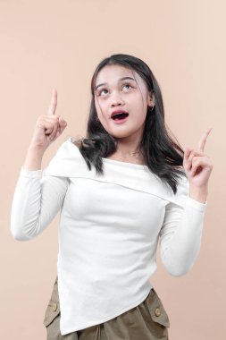 Şaşırmış genç bir Asyalı kadın, iki eliyle işaret ederken, şaşkınlık ve keşif ifade ederken, yeni fikirler, fırsatlar ve ilham kavramları için mükemmel.