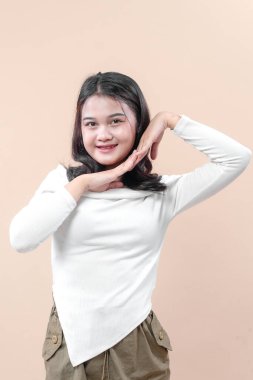 Genç bir Asyalı kadın, elleri çenesinin altında poz verirken ışıl ışıl gülümser. Cazibesini, özgüvenini ve pozitifliğini göstererek zarif ama zarif bir hayat tarzı portresi çizer..