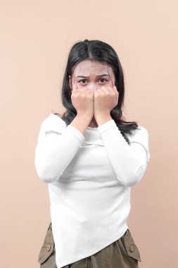 İki eliyle ağzını kapatan sıradan giysili Asyalı bir kadın endişeli ve endişeli bir ifade sergiliyor..