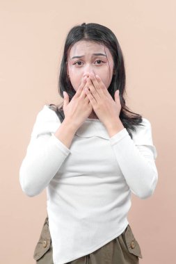 Beyaz bluzlu Asyalı bir kadın iki eliyle ağzını kapatıyor korku, endişe ve hassasiyet taşıyan şok olmuş ve duygusal bir ifade sergiliyor..