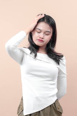 Beyaz bluzlu Asyalı bir kadın kafasına kapalı gözlerle dokunuyor. Stresli ve yorgun bir ifade sergiliyor. Baş ağrısını, hayal kırıklığını veya duygusal yorgunluğu yansıtıyor..