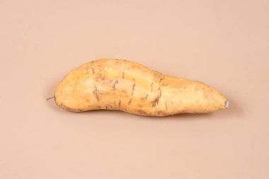 Cilembu tatlı patatesine yakın plan, sade arka planda doğal dokusu olan, eşsiz şeklini, topraksı yüzeyini ve sağlıklı bir tropikal gıda malzemesi olarak potansiyelini gösteren.