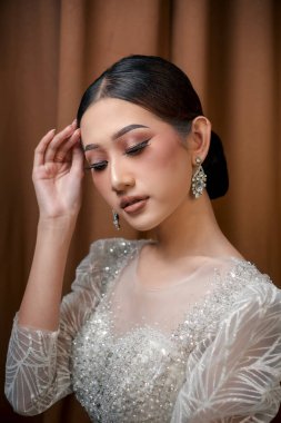 Zarif Endonezya makyaj portresi ışıl ışıl beyaz bir elbise içinde, kusursuz bir cilt, göz kamaştırıcı bir makyaj, zarif küpeler, ve yumuşak büyüleyici bir poz.