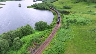 Hogwarts Ekspres treni bir su kütlesinin yanındaki raylarda ilerliyor. Tren siyah ve kırmızı.