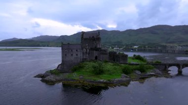 Bir İskoç şatosu bir su kütlesine bakan bir tepededir. Kale yemyeşil bir araziyle çevrili.