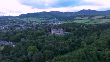 Ortasında İskoç şatosu olan büyük yeşil bir orman. Şato ağaçlarla çevrili ve bir vadinin ortasında yer alıyor.
