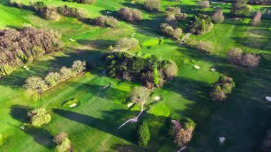 Baharda ağaçlarla çevrili delikler üzerinde uçan yeşil golf sahası yüksek insansız hava aracı görüntüsü