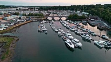 Nehrin üzerinde süzülen havadan bir açı ve yazın günbatımında, nehir kenarında, ağaçlarla çevrili bir köprü.