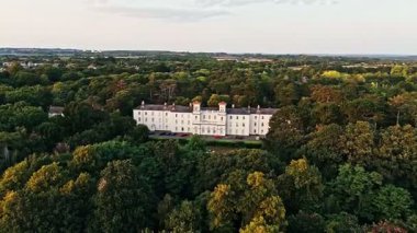 İngiliz Beyaz Malikanesi 'nin üzerinde uçan hava aracı vuruldu. Etrafı yazın günbatımında ağaçlarla çevrili.