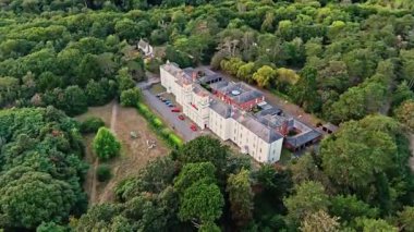 Uçan İHA Yazın günbatımında ağaçlarla çevrili İngiliz Beyaz Konağı üzerinde uçarken çapraz çekim