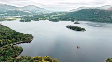 İngiltere Göl Bölgesi 'ndeki Ullswater Gölü' nde, ağaçlarla, doğayla, vadilerle ve dağlarla kaplı adalarda yaz mevsiminde bulutlarla uçan ve dönen hava aracı görüntüleri.