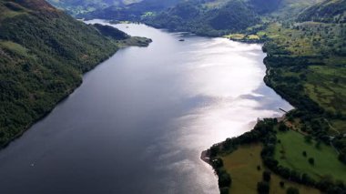 Yazın İngiltere Göl Bölgesi 'nde çim ve ağaçlarla kaplı dağ vadisinde, Urallar Gölü' nün üzerinden uçan insansız hava aracı görüntüleri.