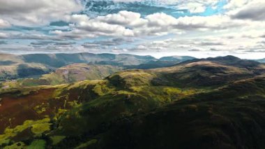 İngiltere Göl Bölgesi 'nde çimen ve ağaçlarla kaplı dağların ve tepelerin solundan çekilen hava aracı sesleri yaz aylarında mavi bulutlu gökyüzü ile