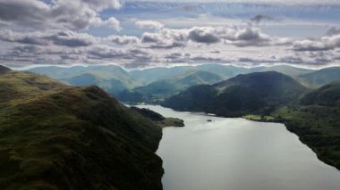 Yazın İngiltere 'nin göl bölgesinde ağaçlarla ve otlarla kaplı tepelerle kaplı dağ vadisi içinde göl üzerinde hava aracı görüntüsü bırakıldı.