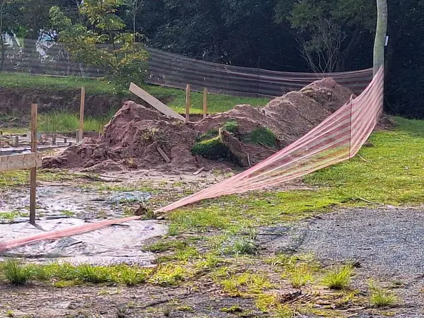 İlerleyen bir inşaat sahasında toprak yığını ve kırmızı güvenlik bariyerleri olan bir toprak çalışma alanı yer alıyor. Alanı ve bazı inşaat malzemelerini gösteren işaretler var. Çevreleyen bitki örtüsü doğal bir kontrastı da ekliyor..
