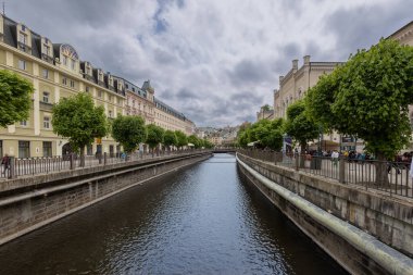 Karlovy Vary 'deki Tepla Nehri boyunca gezinti. Tepla Nehri 'nin her iki yakasında, Karlovy Vary' nin göbeğinde, pastel renkli tarihi binalarla çevrili geniş bir yaya geçidi uzanır.