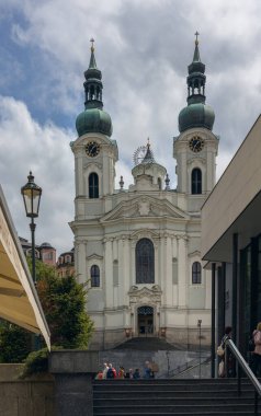 Karlovy Vary 'deki St. Mary Magdalene Kilisesi, 30 Nisan 2024. Karlovy Vary 'deki St. Mary Magdalene Kilisesi' nin Barok ihtişamı kestane ağacının açtığı karamsar gökyüzüne karşı görkemli bir şekilde duruyor.