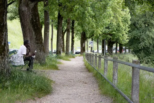Bern, İsviçre, 20 Haziran 2024. İsviçre, Bern 'de gölgeli yürüyüş yolu boyunca uzun ağaçların altında bir bankta oturan bir adam. Sakin atmosfer doğal yeşillik ve kırsal eskrim ile zenginleşir.