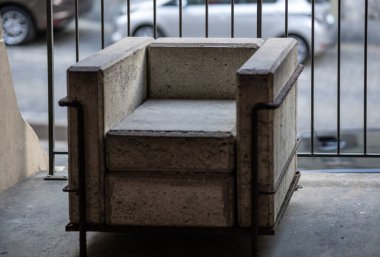 Bern, İsviçre, 20 Haziran 2024. Tamamen betondan ve metalden yapılmış eşsiz bir koltuk sakin bir şehir caddesine bakan balkon ya da terasta duruyor. Sanayi estetiği ve ham dokular