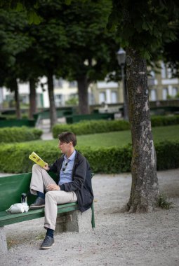  Bern, İsviçre, 20 Haziran 2024. Huzurlu bir şehir parkında yeşil bir bankta oturan bir adam, bir kitap okumaya dalmış..
