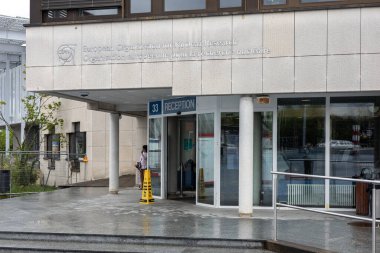 Ziyaretçiler, CERN 'in modern dairesel binalarının önünden bulutlu gökyüzünün altında yürüyorlar.. 