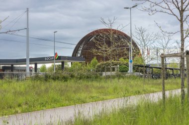 CERN 'deki Bilim ve Yenilik Küresi bayrak direkleri ve bulutlu bir gökyüzünün altında bir tramvay durağının arkasında belirgin bir şekilde duruyor. 20 Haziran 2023. Yüksek kalite fotoğraf