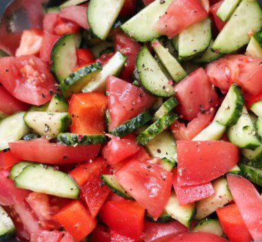 Dilimlenmiş domateslerden yapılmış taze sebze salatası, salatalık ve dolmalık biber, üzerine karabiber serpiştirilmiş. Sağlıklı ve renkli bir yemek, dengeli bir diyet, vejetaryen yemekleri veya yaz tarifleri için mükemmel..