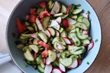 Bir kasede taze sebze salatası. İçinde çıtır salatalık, canlı turp ve yeşil soğan var..
