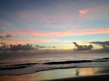 Pembe, turuncu ve mavi tonlarını da içeren ve ufukta huzurlu ve sakin bir atmosfer yaratan, gökyüzünün canlı renklerini yansıtan sakin bir okyanusla huzurlu bir gün batımı..