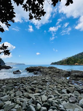 Kayalık kıyı şeridi, açık mavi gökyüzü ve uzak tepeleri olan manzaralı bir kıyı manzarası. Batu Sahili Yeşil Koyu, Banyuwangi