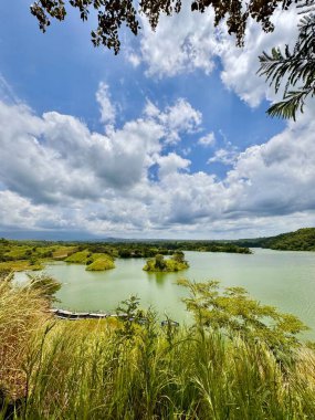 Bulutlu bir gökyüzünün altında yemyeşil bir göl ve küçük adaların manzarası. Bajulmati Barajı Situbondo