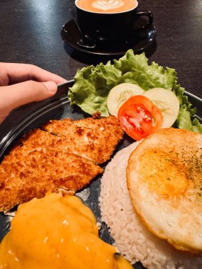 Bir tabak kızarmış tavuk katsusu, pilav, sahanda yumurta ve salata, yanında da bir fincan latte ile latte sanat..