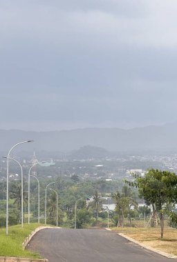 Bereketli yeşil bir vadiye doğru uzanan dolambaçlı bir yolun manzarası. Uzak dağlar sisle kaplanmış. Sokak lambaları yolda, ve ağaçlar kenarlarda görünüyor..