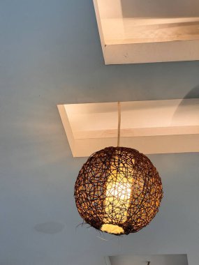 Yumuşak mavi arka planı olan bir tavandan sarkan dokuma malzemeden yapılmış dekoratif bir kolye ışığı. Işık sıcak bir parıltı yayar, rahat bir atmosfer yaratır..