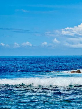 Küçük okyanus dalgalarıyla deniz manzarası ve tropik bir ortamda bulutlarla dağılmış mavi gökyüzü.
