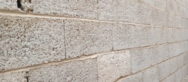 Görünür havan hatları ve pürüzlü yüzey detaylarıyla desenli beton blok duvarın yakın görüntüsü. Duvarın bir bölümünde küçük bir çatlak beliriyor..