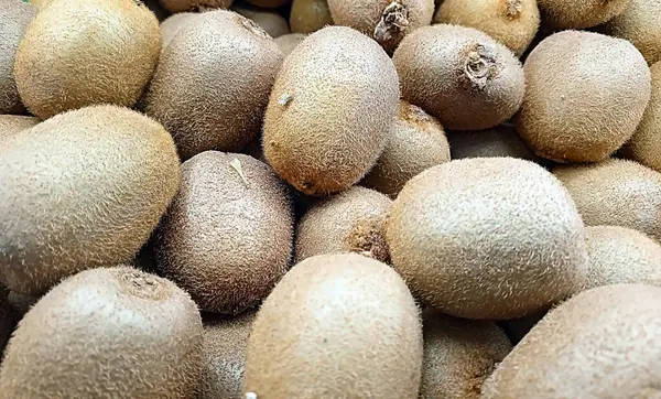 Tüylü kahverengi tenli kivi meyveleri yığını, doğal ışık altında yakalanmış, sağlıklı gıda, pazar üretimi veya tropikal beslenme temalarını sergilemek için ideal..