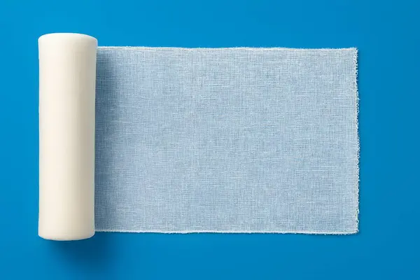 Kısmen açılmış açık mavi gazlı bez rulosu, solunabilir yara bandını, steril bakımı ve klinik hijyeni simgeliyor..