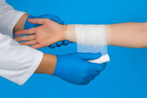 Eldivenli ellerin ön koluna sarılı olması, steril sağlık ortamındaki yara bakımını, hijyeni ve klinik tekniği sembolize ediyor..