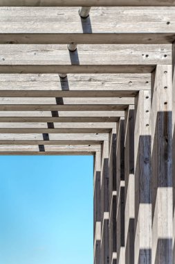 Geometrik desenli Modern Tahta Kiriş Yapısı ve Açık Mavi Gök Altındaki Gölgeler.