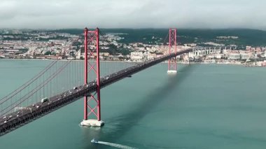 Portekiz 'in Lizbon kentindeki 25 de Abril Köprüsü' nün Tagus Nehri 'ni şehir manzarası ve trafiği ile kaplayan çarpıcı bir zaman atlaması. Lizbon, Portekiz, 16 Aralık 2023