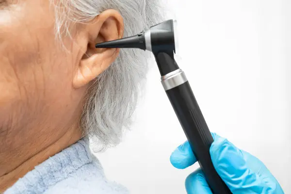 Otolaryngologist ya da ENT hekim doktoru yaşlı hasta kulağını otoskopla muayene ediyor, işitme sorunu var..