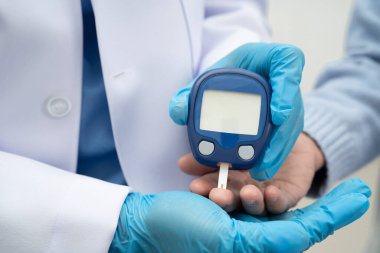 Diyabet tedavisinde kan şekeri seviyesini kontrol etmek için dijital glikoz ölçer kullanan Asyalı doktor.