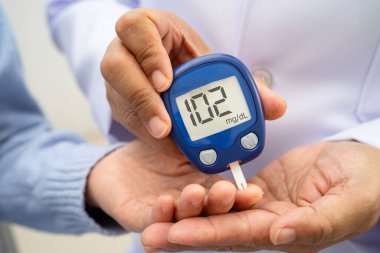 Diyabet tedavisinde kan şekeri seviyesini kontrol etmek için dijital glikoz ölçer kullanan Asyalı doktor.