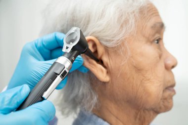 Otolaryngologist ya da ENT hekim doktoru yaşlı hasta kulağını otoskopla muayene ediyor, işitme sorunu var..