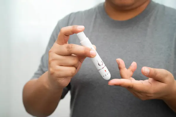 Evde parmak üzerinde dijital mızrakla kan şekeri seviyesini ölçmek için Asyalı kadın kendini test ediyor..