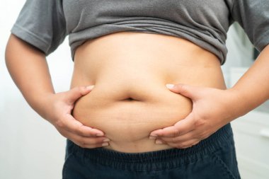 Asyalı kadın şişman göbeğini sıkmak için elini kullanıyor. Büyük boy aşırı kilolu ve obez..