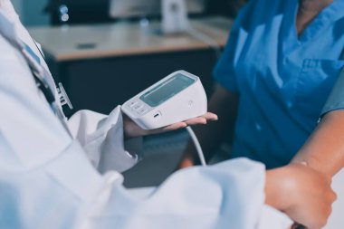 Steteskopla sfenometre kullanan bir doktor hastanede kan basıncını ölçüyor..